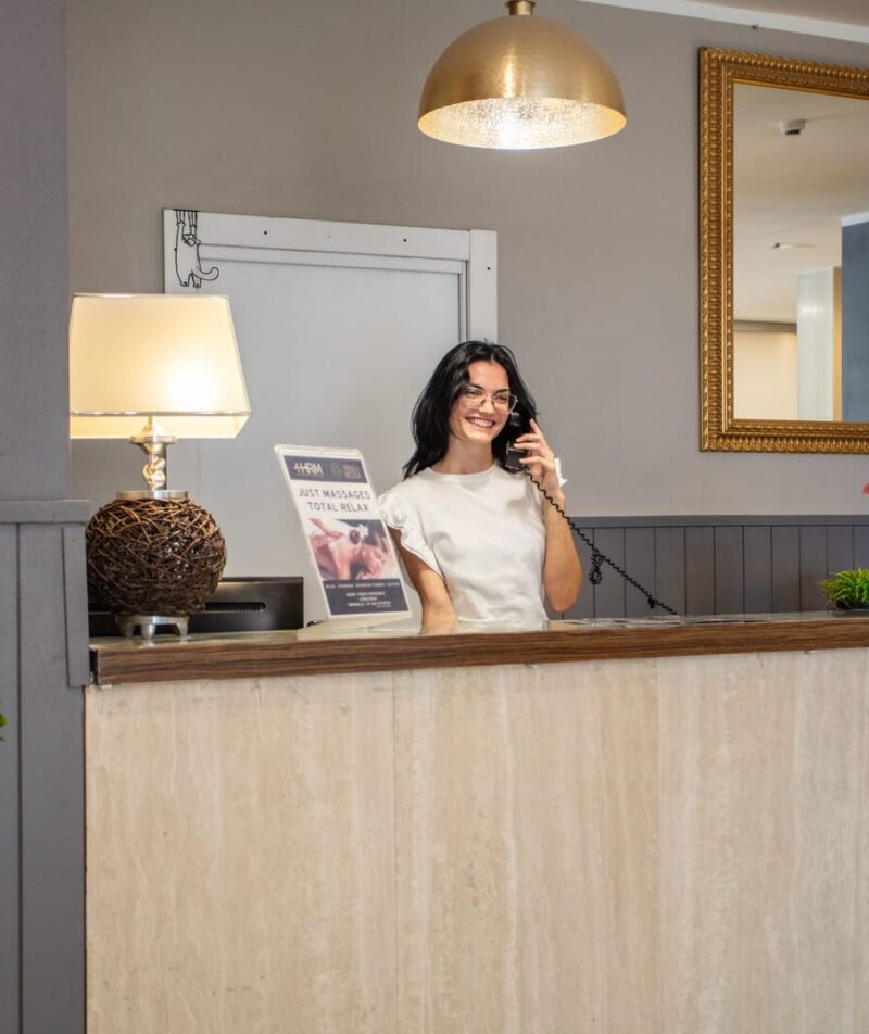 Receptionist al banco, sorridendo mentre risponde al telefono.
